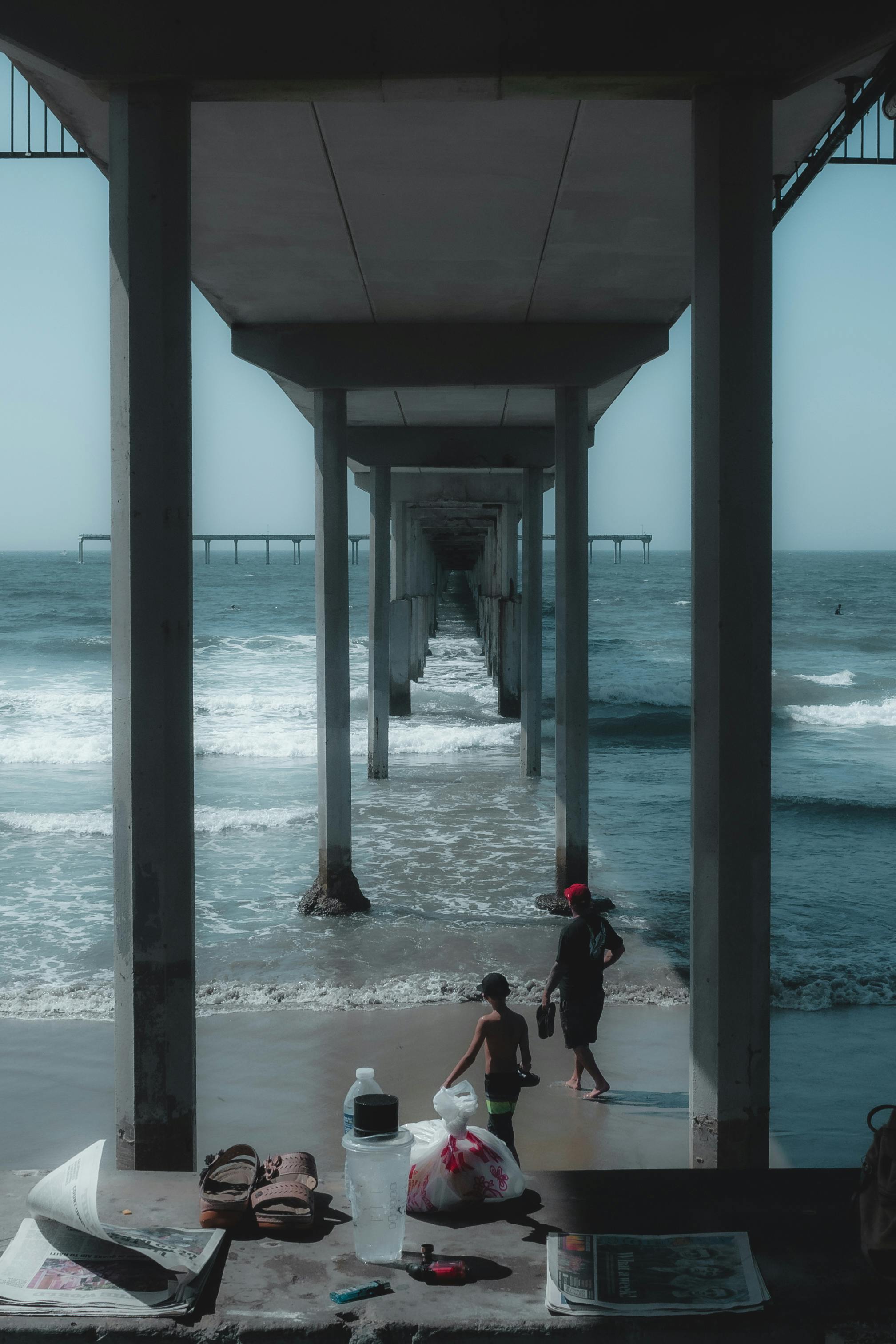 A scenic view of a pier in San Diego with two people walking on the beach beneath it.