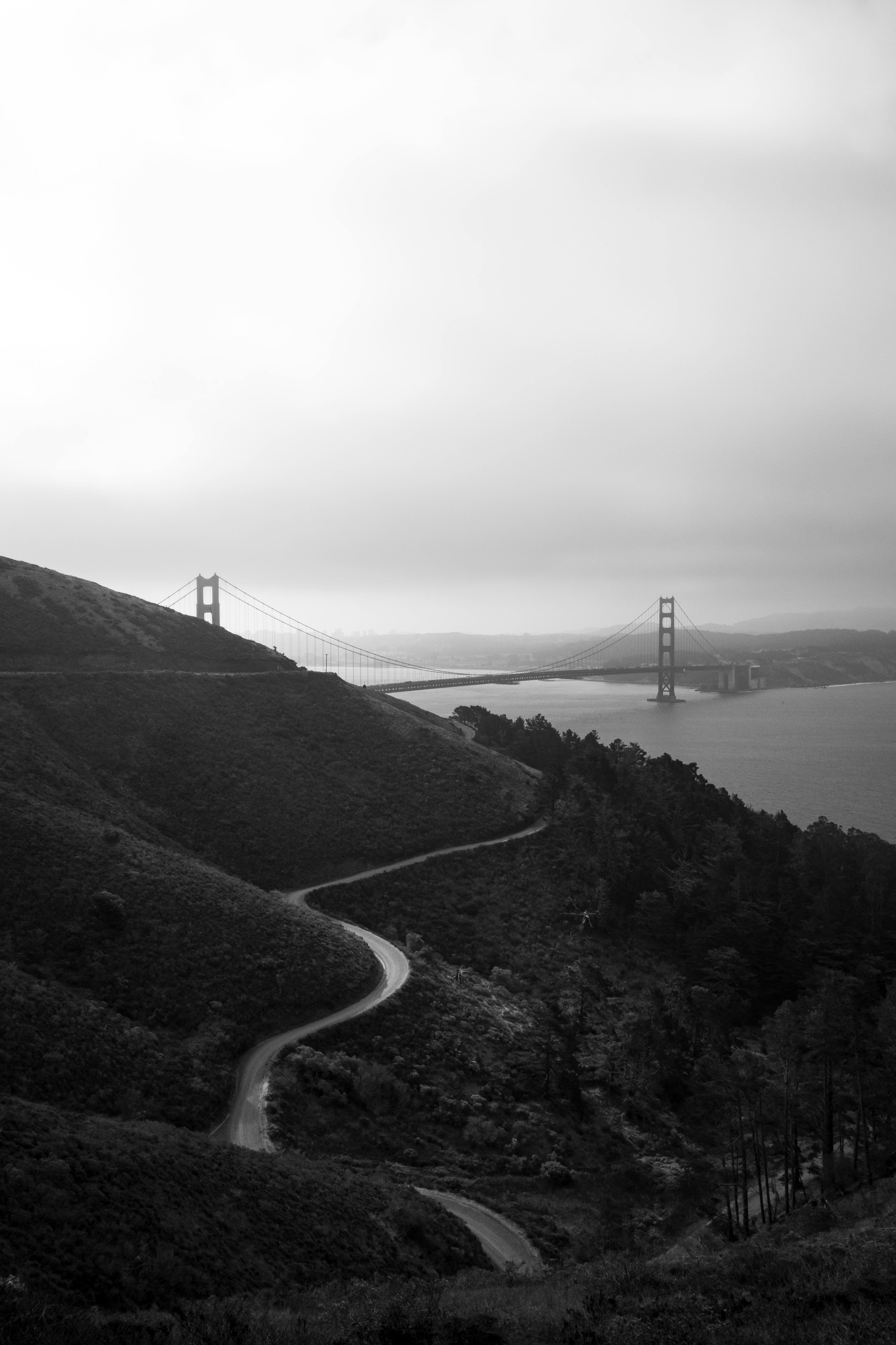 A scenic black and white view of the Golden Gate Bridge from a winding hillside road.
