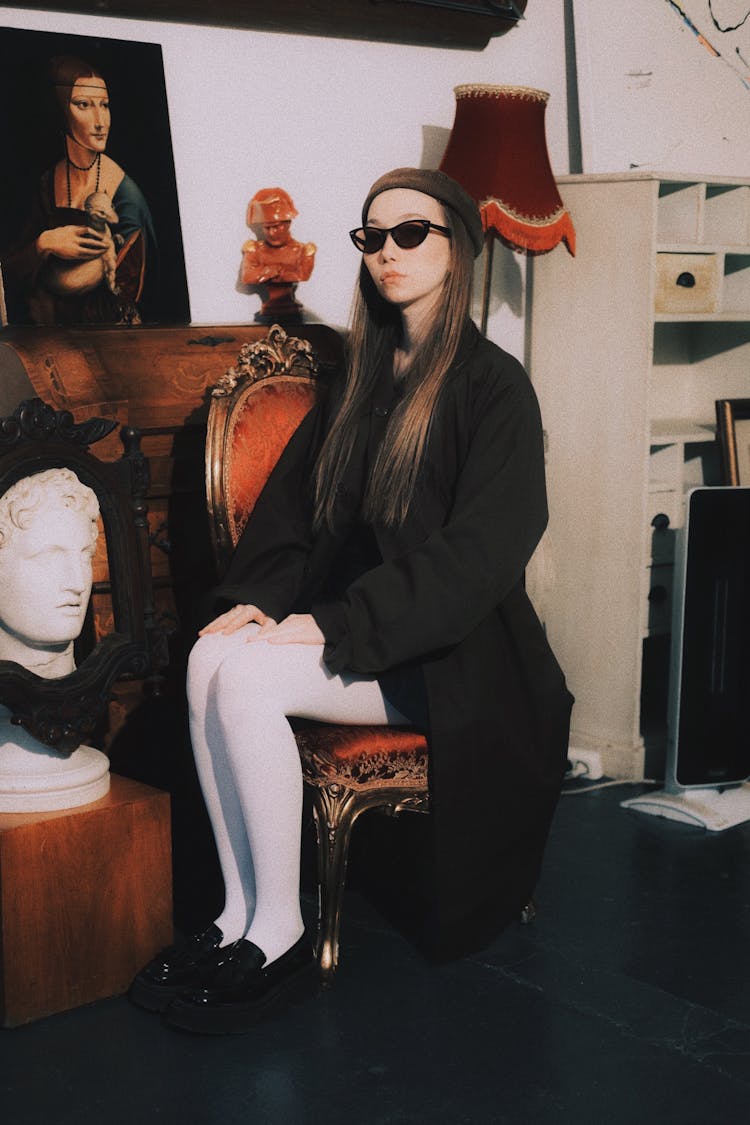 Woman Sitting In Black Clothes, Hat And Sunglasses