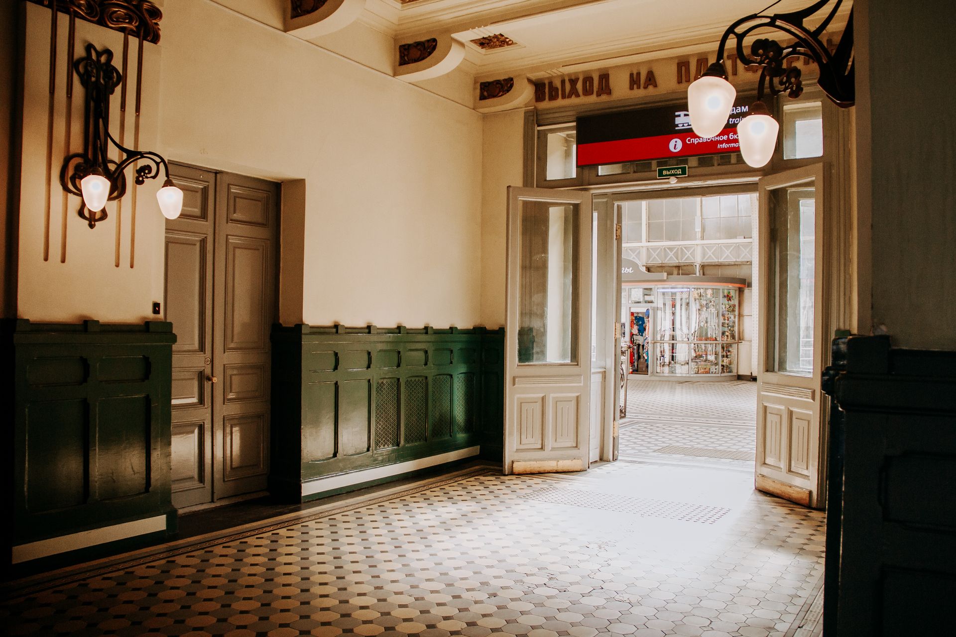 Elegant vintage hallway with intricate lighting and open door leading to an outdoor view.