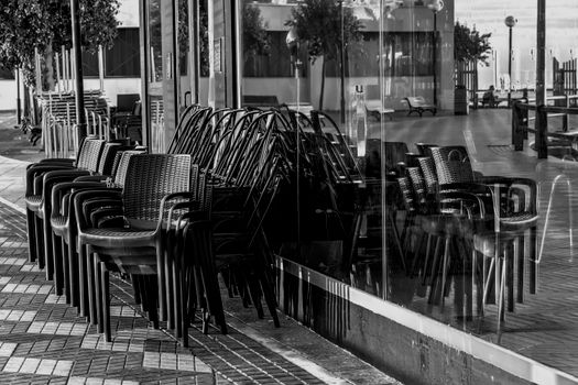 A street scene in Alicante featuring stacked chairs and reflections in a window in black and white.
