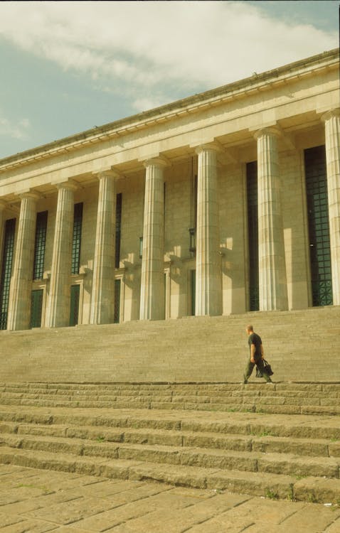 A man walking down the steps of a building with a large building in the background