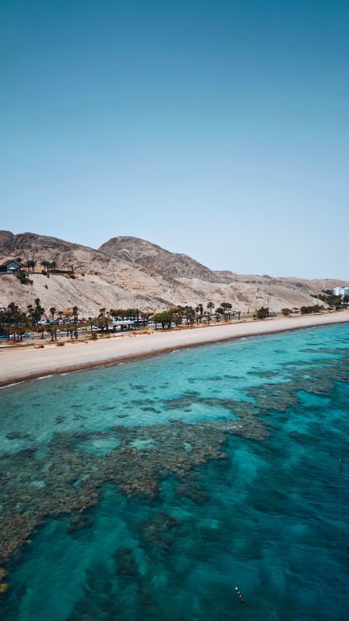 Free A stunning coastline with clear water, coral reef, and mountains under a clear blue sky. Stock Photo