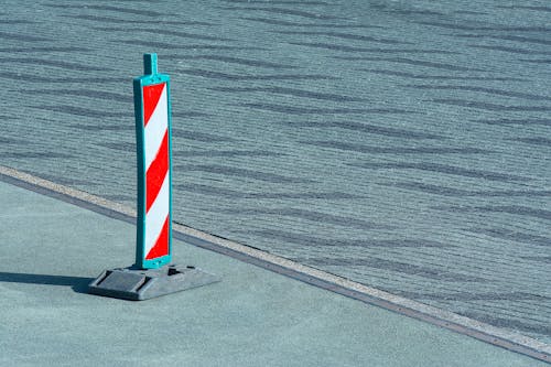 A red and white striped traffic cone sitting on a sidewalk