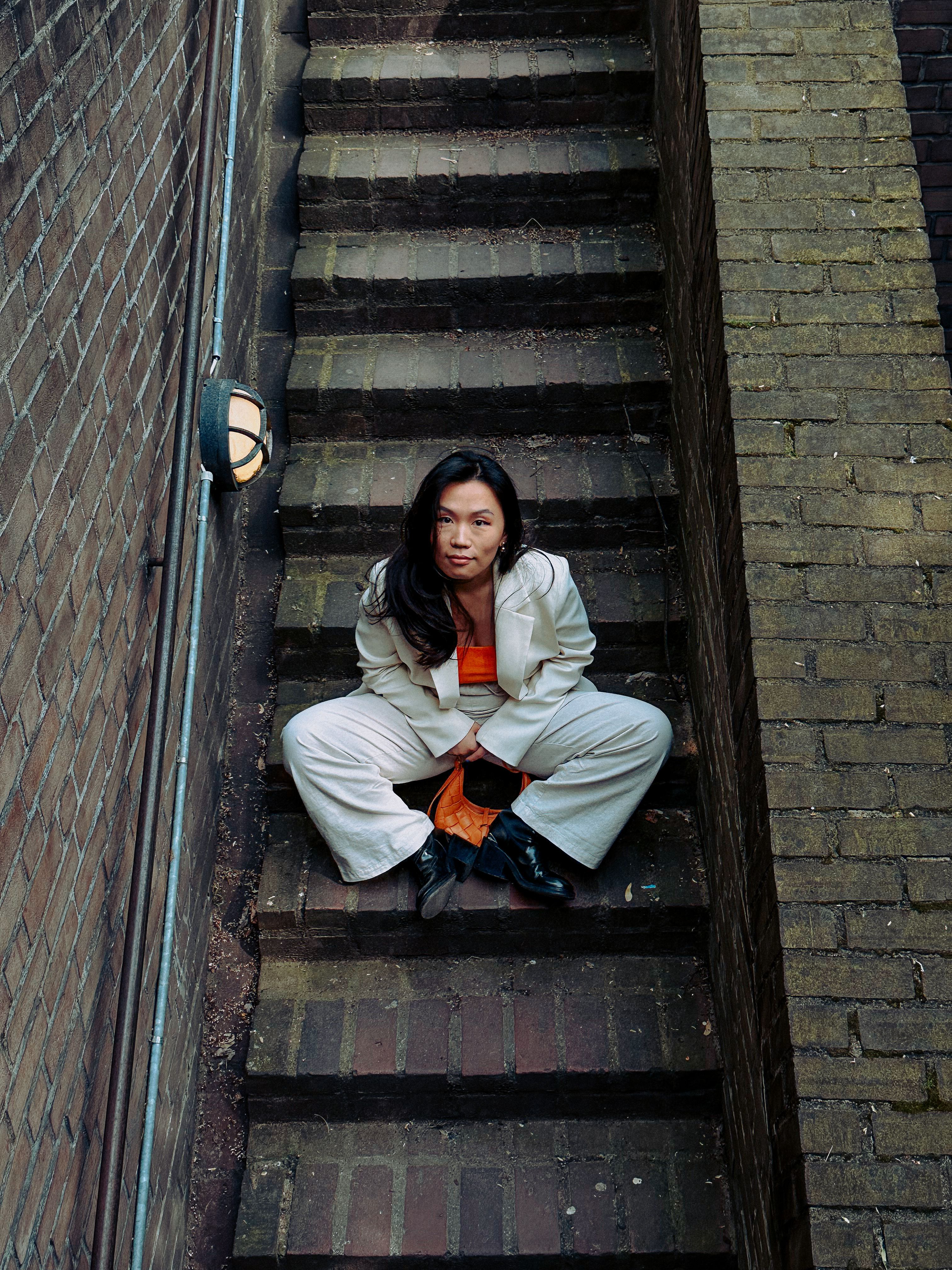 Fashionable woman in a white suit sitting on brick stairs in Cologne, Germany.