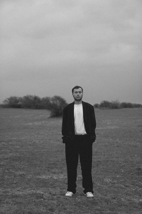 Free A man in a stylish outfit stands in a rural field, captured in black and white photography. Stock Photo