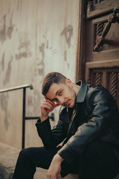 A man in a leather jacket sitting on the steps