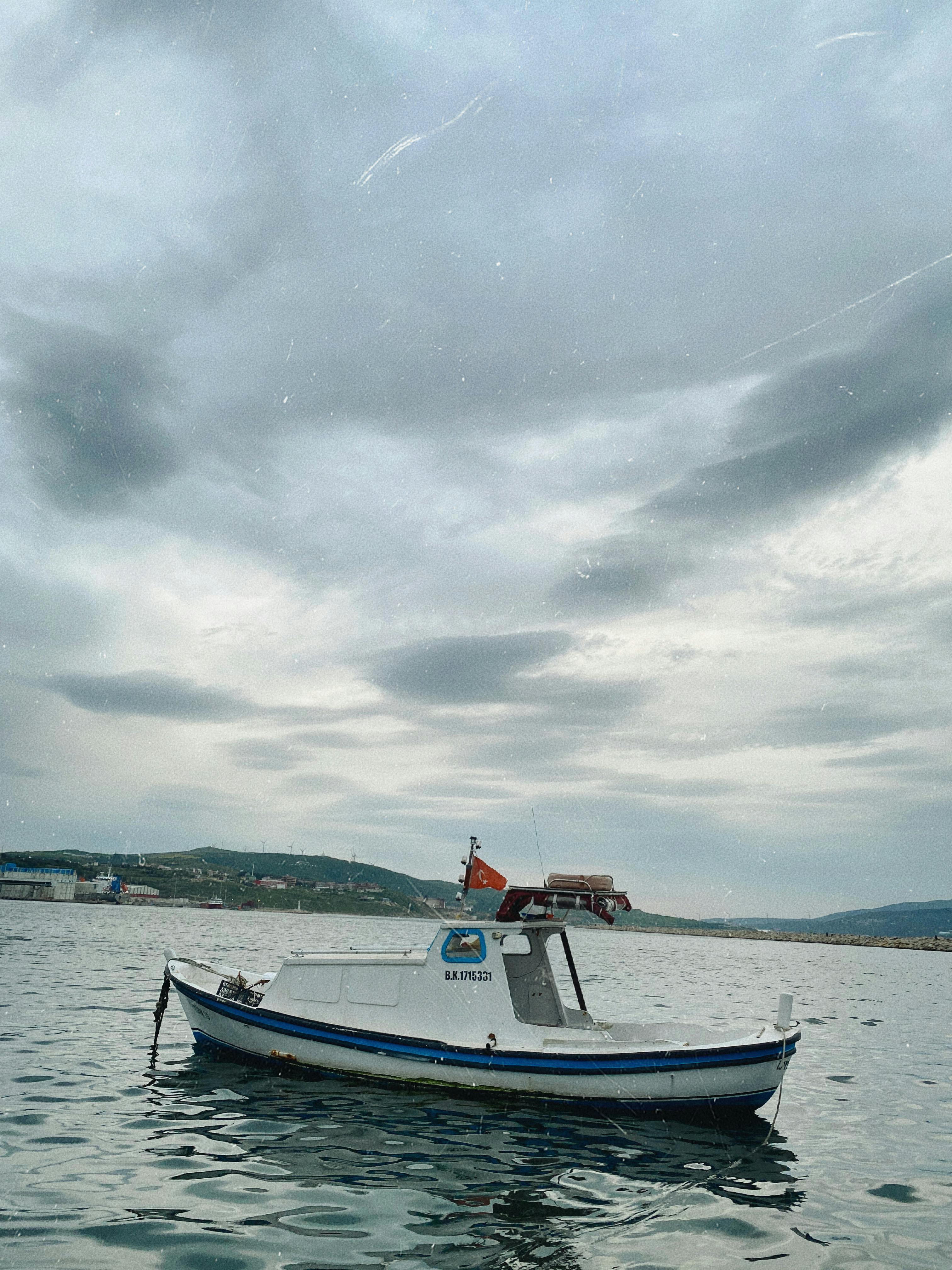 A lone motorboat floats on calm waters under a cloudy Turkish sky, offering a serene coastal view.