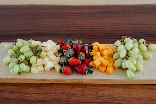 A wooden cutting board with fruit and cheese
