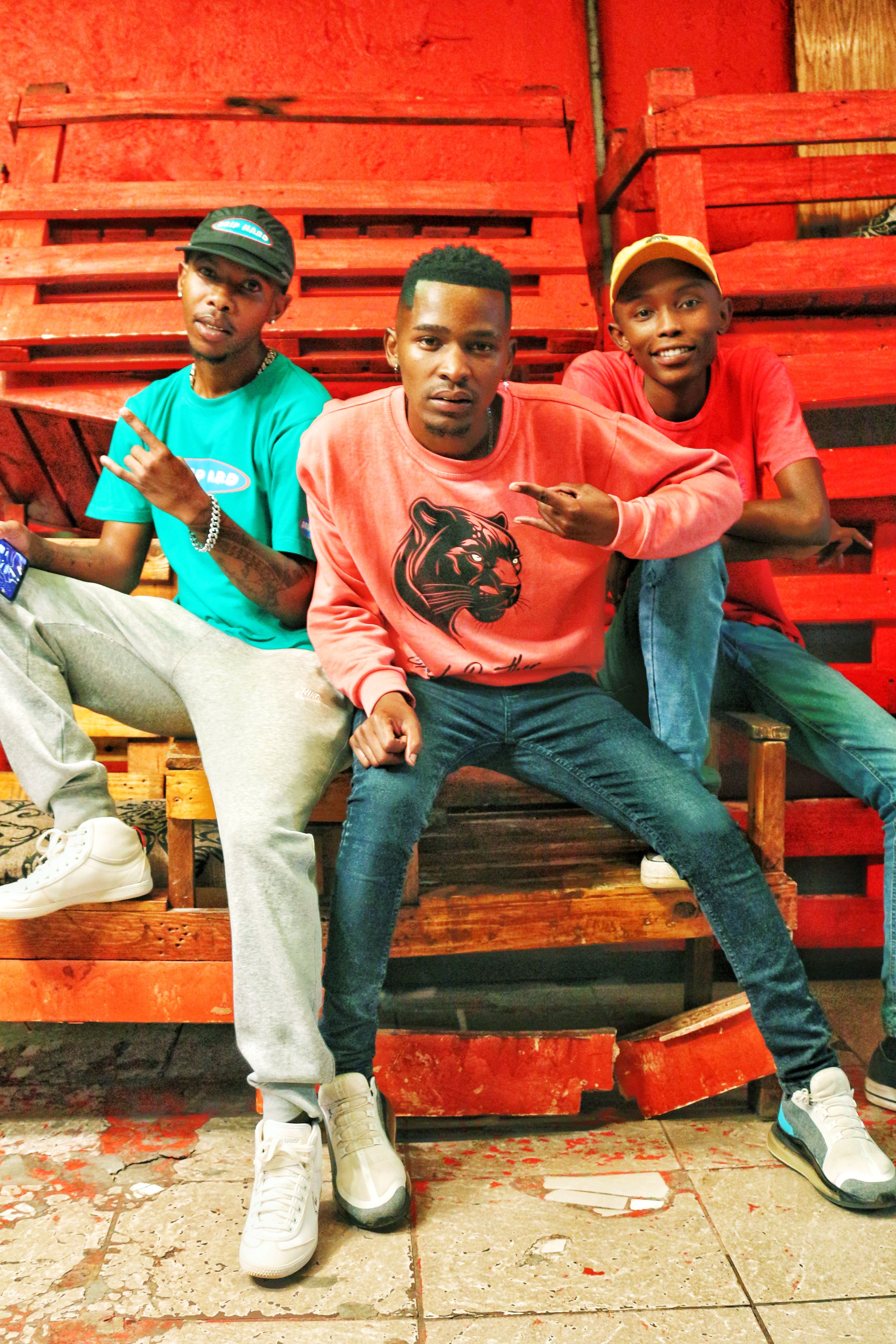 Three young men in casual clothes posing confidently on wooden pallets.