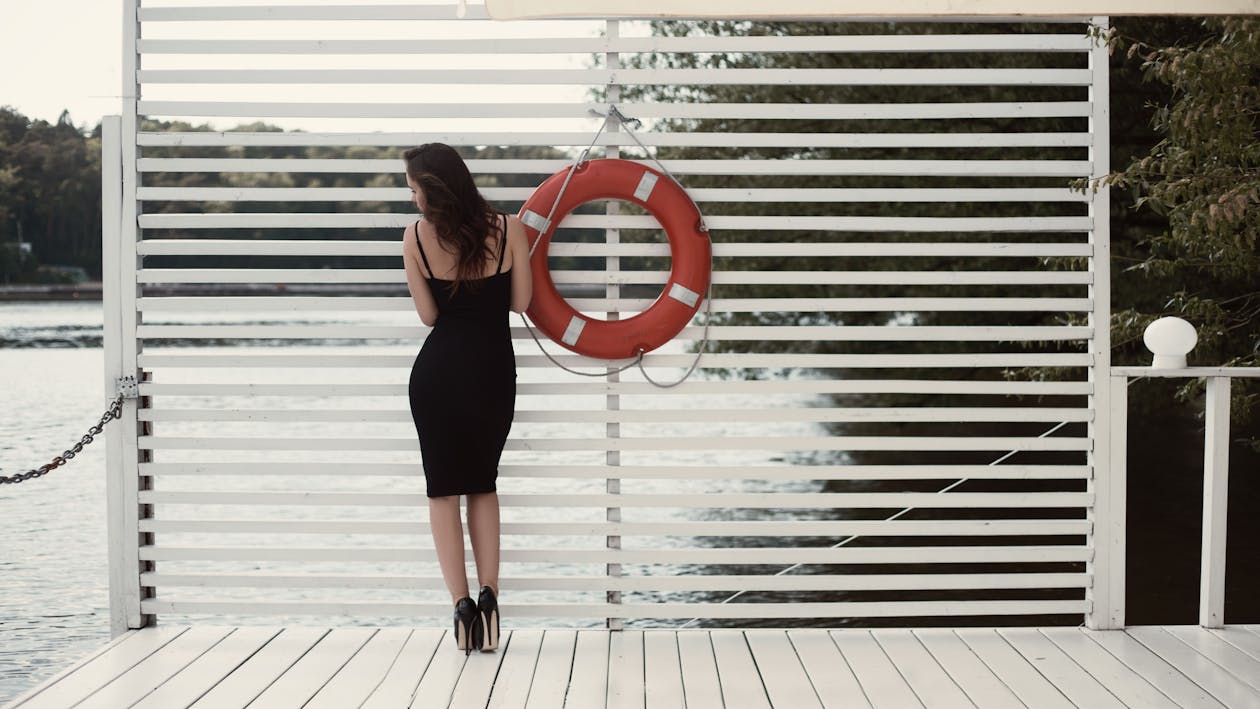 無料 ドックの浮き輪の横にある黒いシースドレスの女性 写真素材