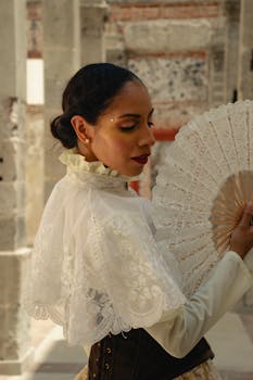 A woman in a lace blouse holding a fan, exuding elegance in a historic setting.