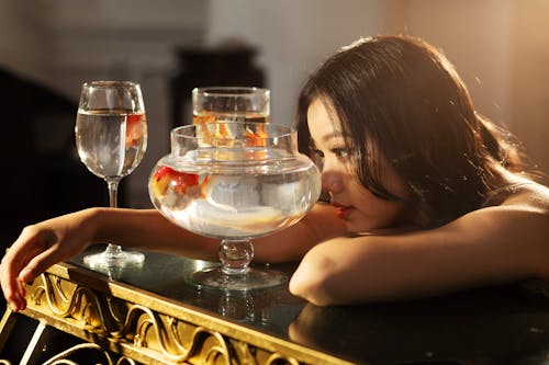 A woman is sitting on a table with a glass of water and a fish bowl