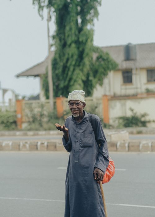 Free Elderly man in traditional attire standing on a street in Ibadan, Nigeria, with houses and trees in the background. Stock Photo