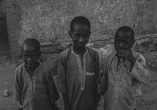 A candid black and white image of three children smiling in a rustic setting.