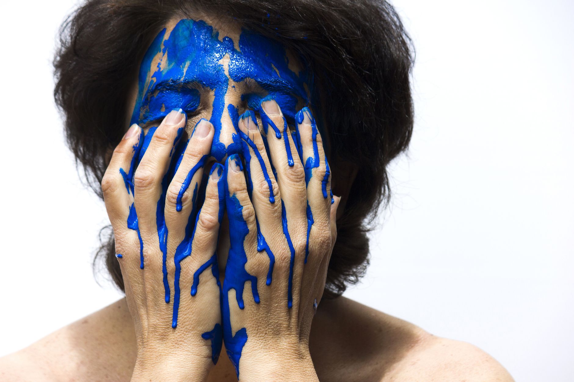 A striking artistic portrait of a woman covered in blue paint, expressing emotion and creativity.