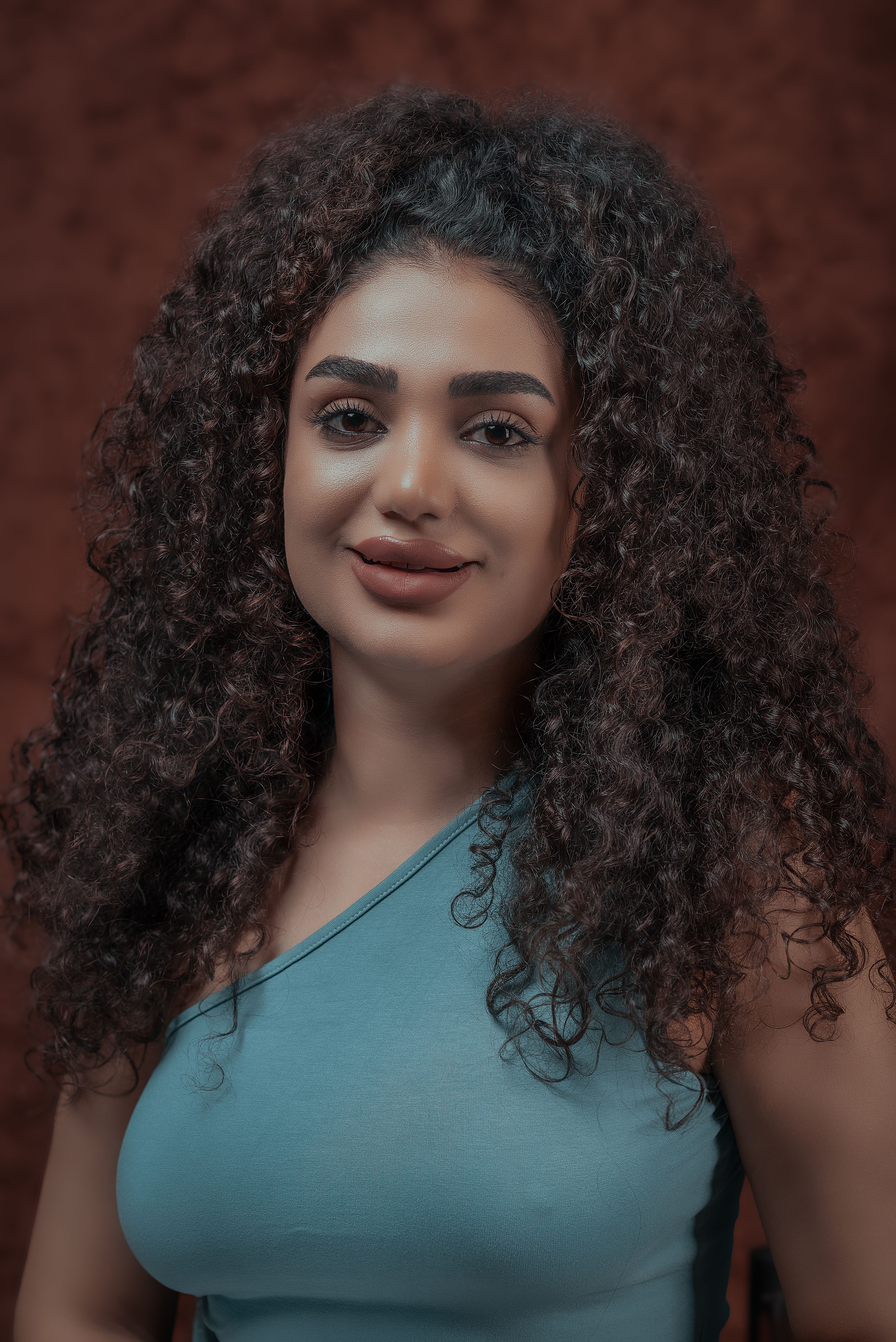 Studio portrait of a young woman with curly hair and a blue top, smiling confidently.