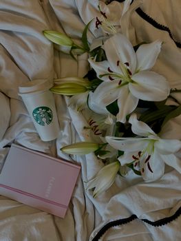 A peaceful setup with lilies, a journal, and a Starbucks cup on a bed.