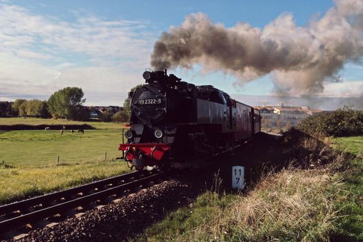 Vintage steam train travels through rural landscape with smoke billowing into the sky.