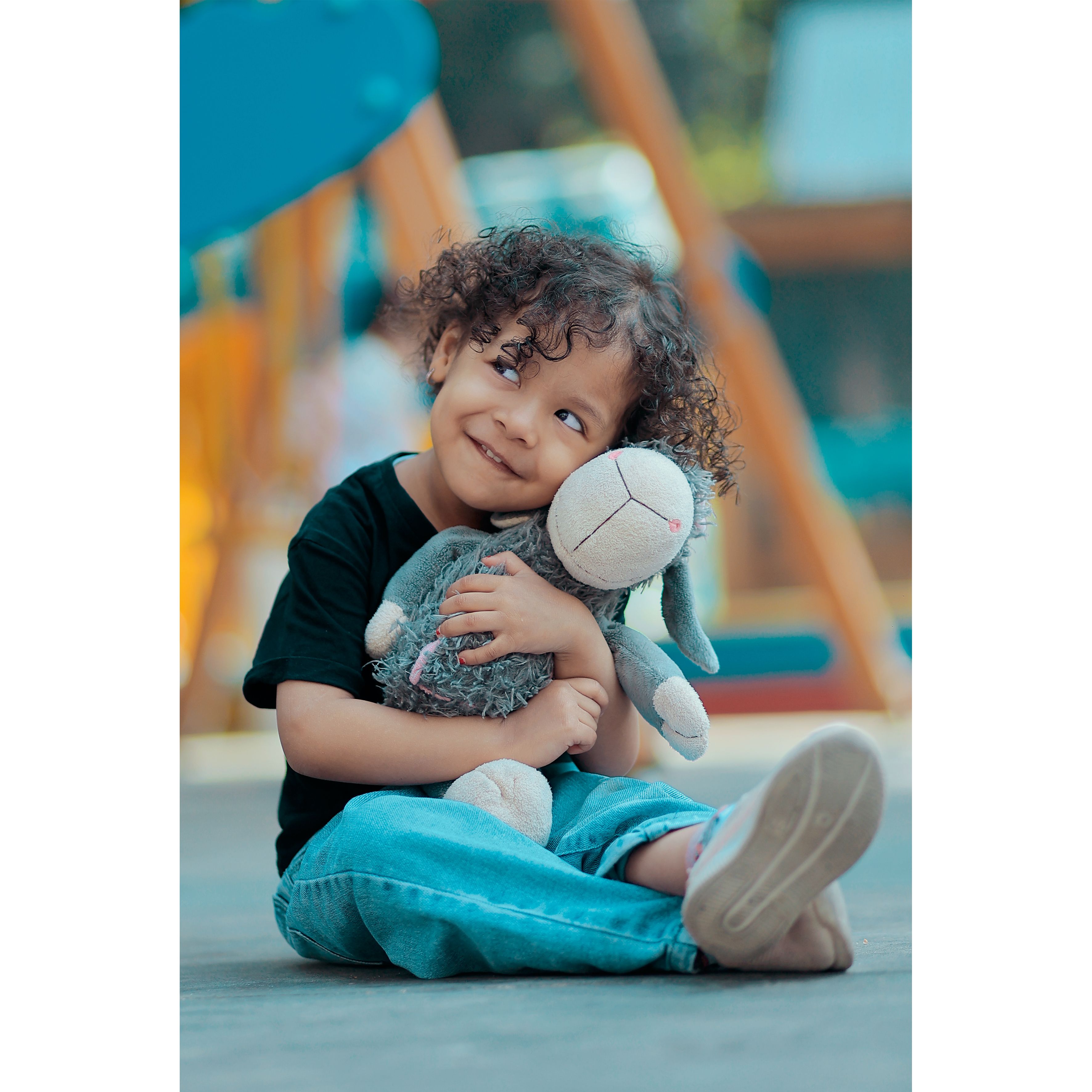 A joyful child with curly hair hugs a plush toy outdoors, radiating happiness and innocence.