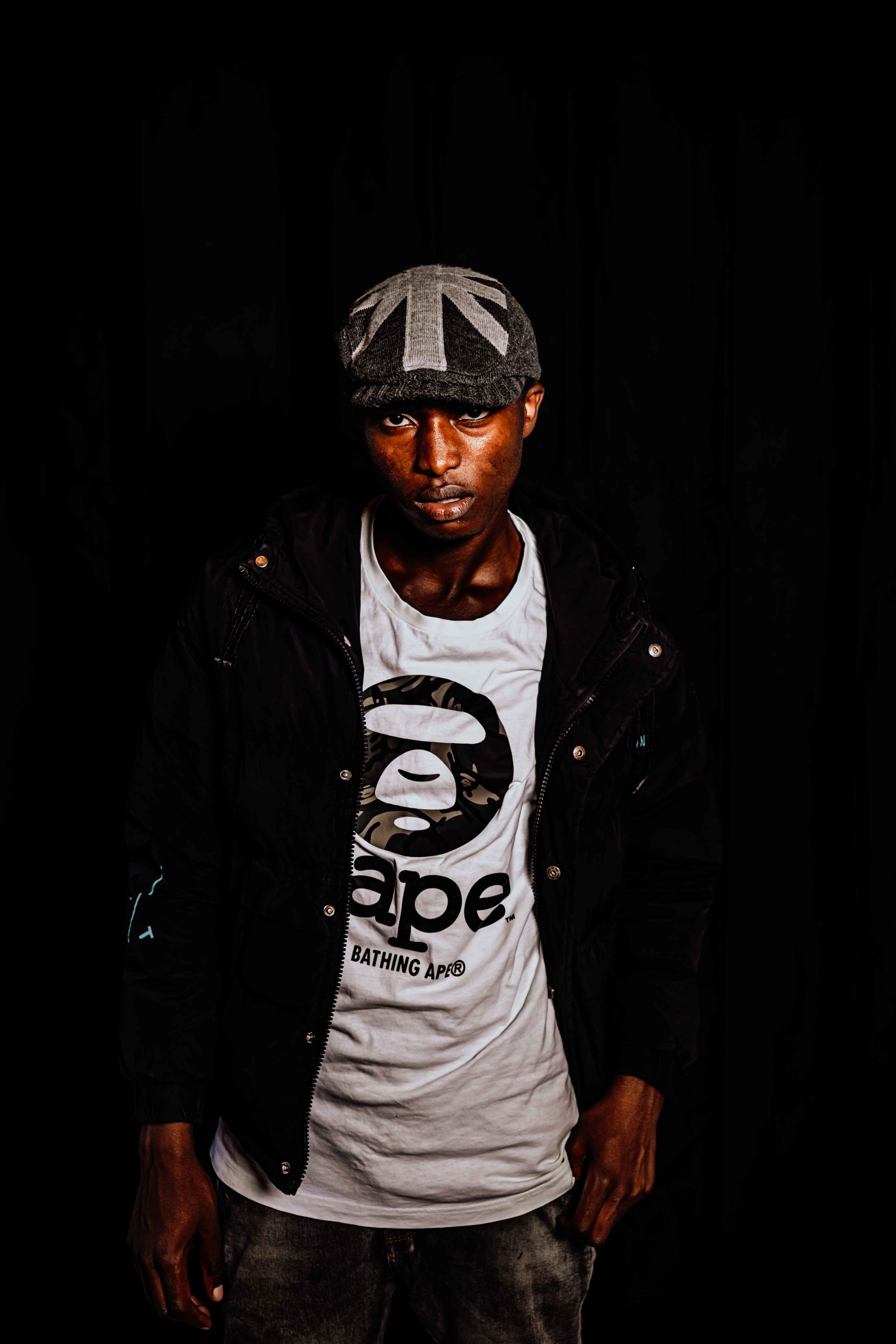 Fashion portrait of a man wearing streetwear with a bold hat, set against a black background.