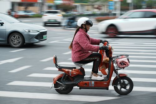 Free Woman in helmet riding motor scooter crossing a city street at pedestrian crossing. Stock Photo