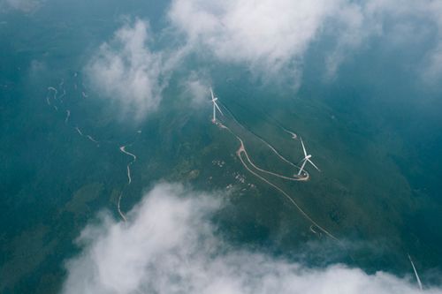 Free Stunning aerial shot showcasing wind turbines amidst lush green landscapes, enveloped by clouds. Stock Photo
