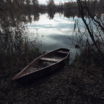 黄昏时分，一艘孤独的独木舟停在波光粼粼的湖边，四周一片静谧