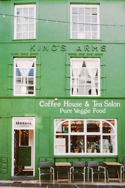 Vibrant green facade of a coffee house and tea salon with outdoor seating and vintage signage.