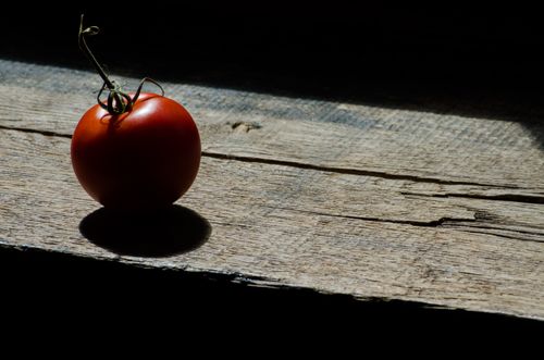 Free A ripe red tomato on a wooden surface, casting a shadow in natural light. Stock Photo