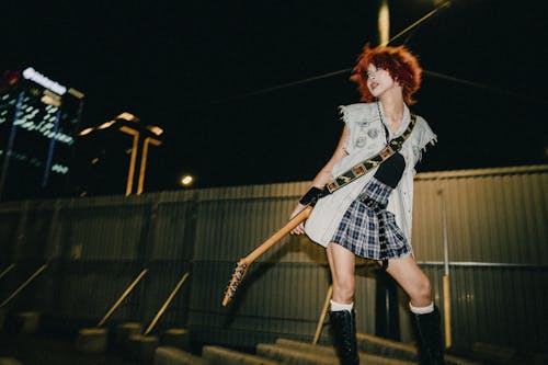 A woman with red hair and a guitar standing on a bridge