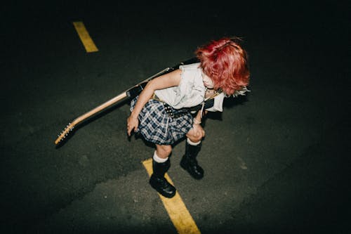 A girl with red hair and a guitar on the ground