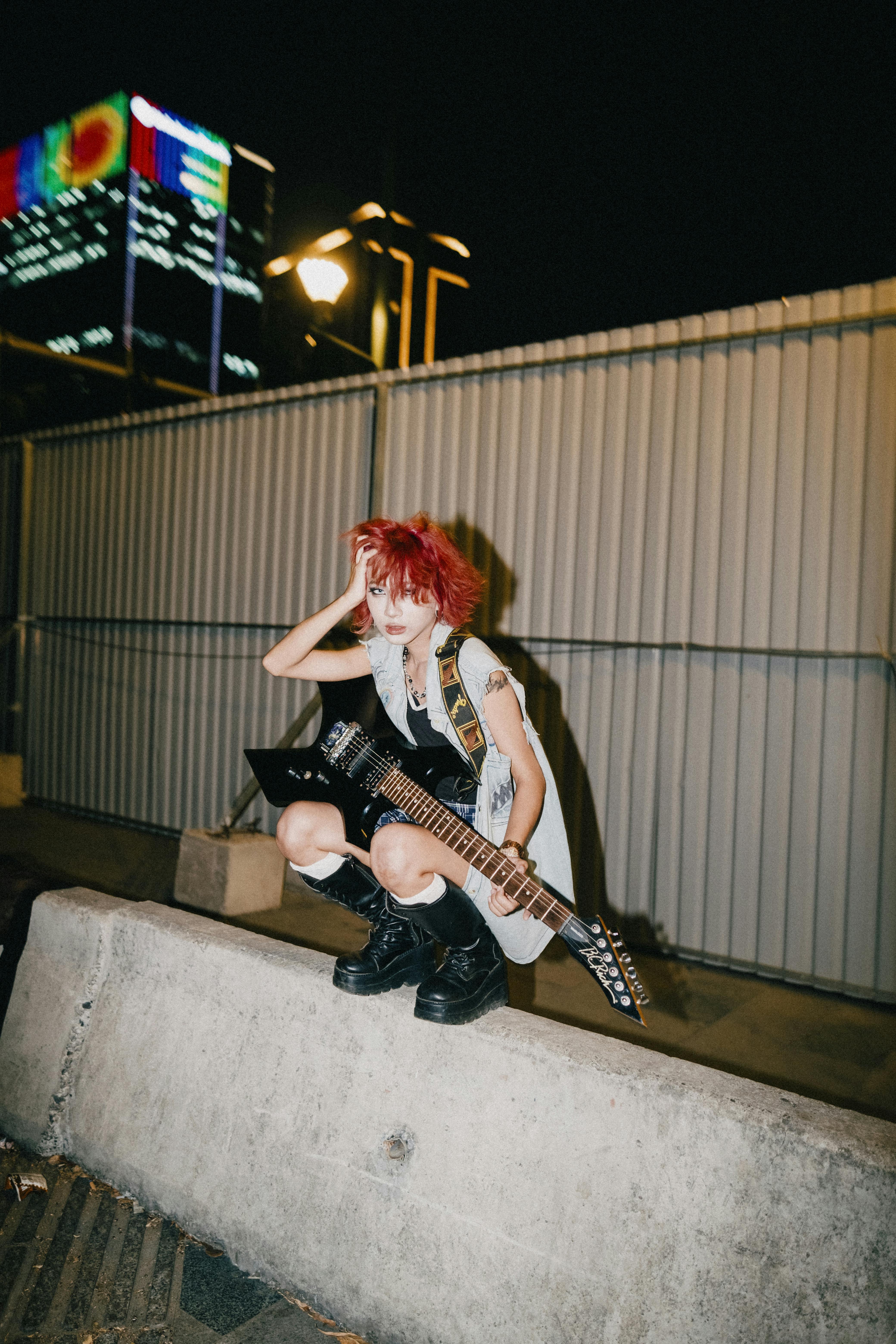 Young punk musician with electric guitar poses energetically at night in an urban environment.