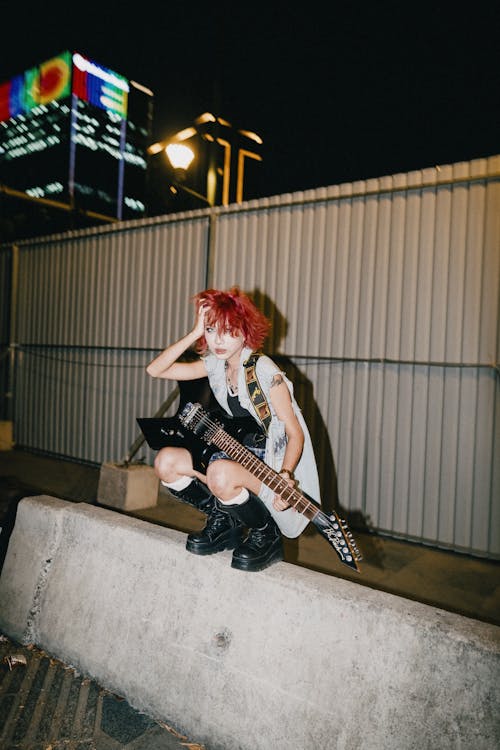A girl with red hair and a guitar sitting on a wall