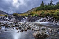 天空多云，宁静的山地景观中，瀑布与溪流在岩石间流淌