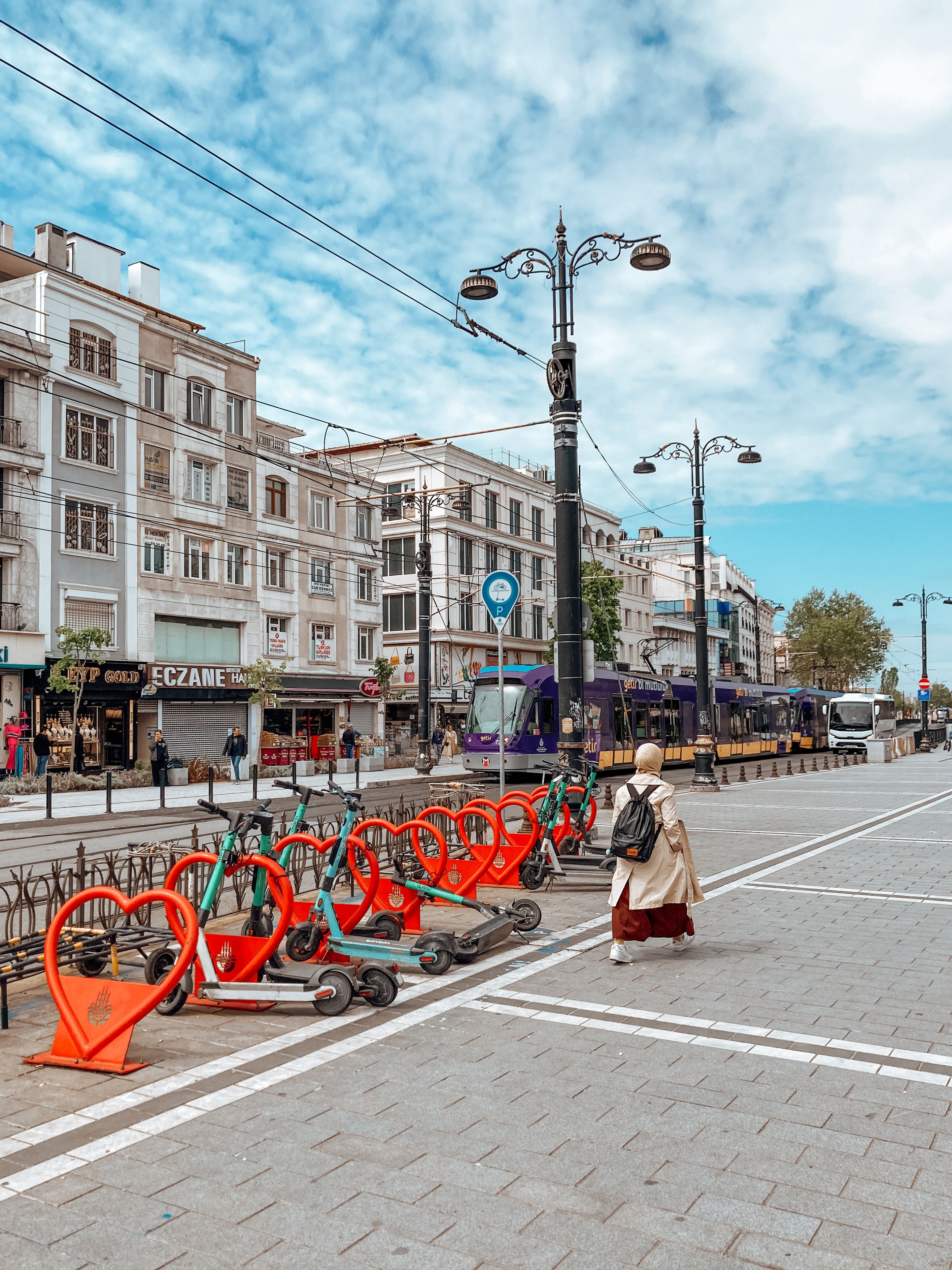 A bustling city street featuring e-scooters, pedestrians, and a tram under a vibrant sky.