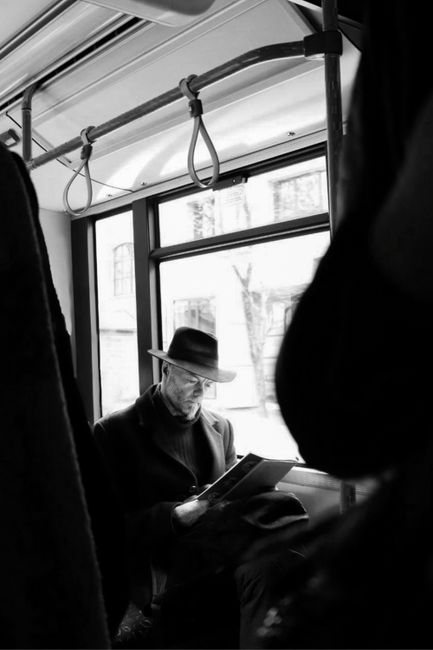 Black and white photo of a man in a hat reading on public transport in Latvia, capturing a moment of elegance.