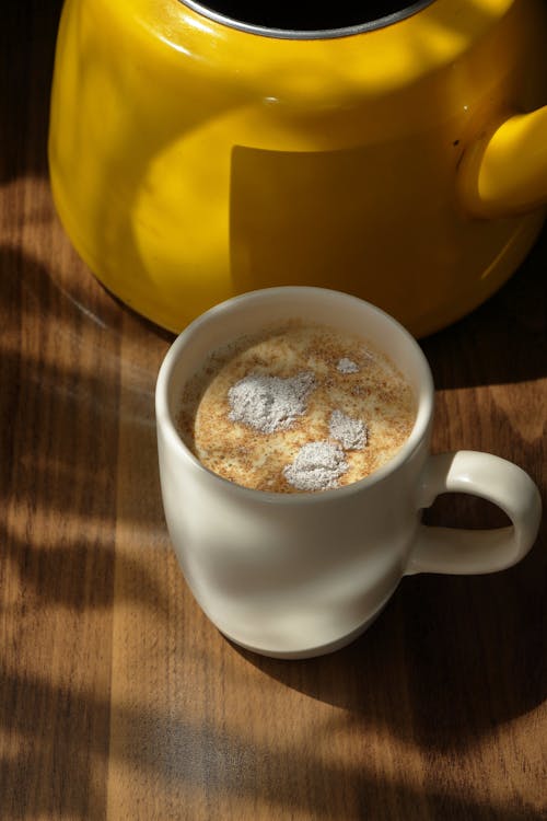 A cup of coffee on a table next to a yellow kettle