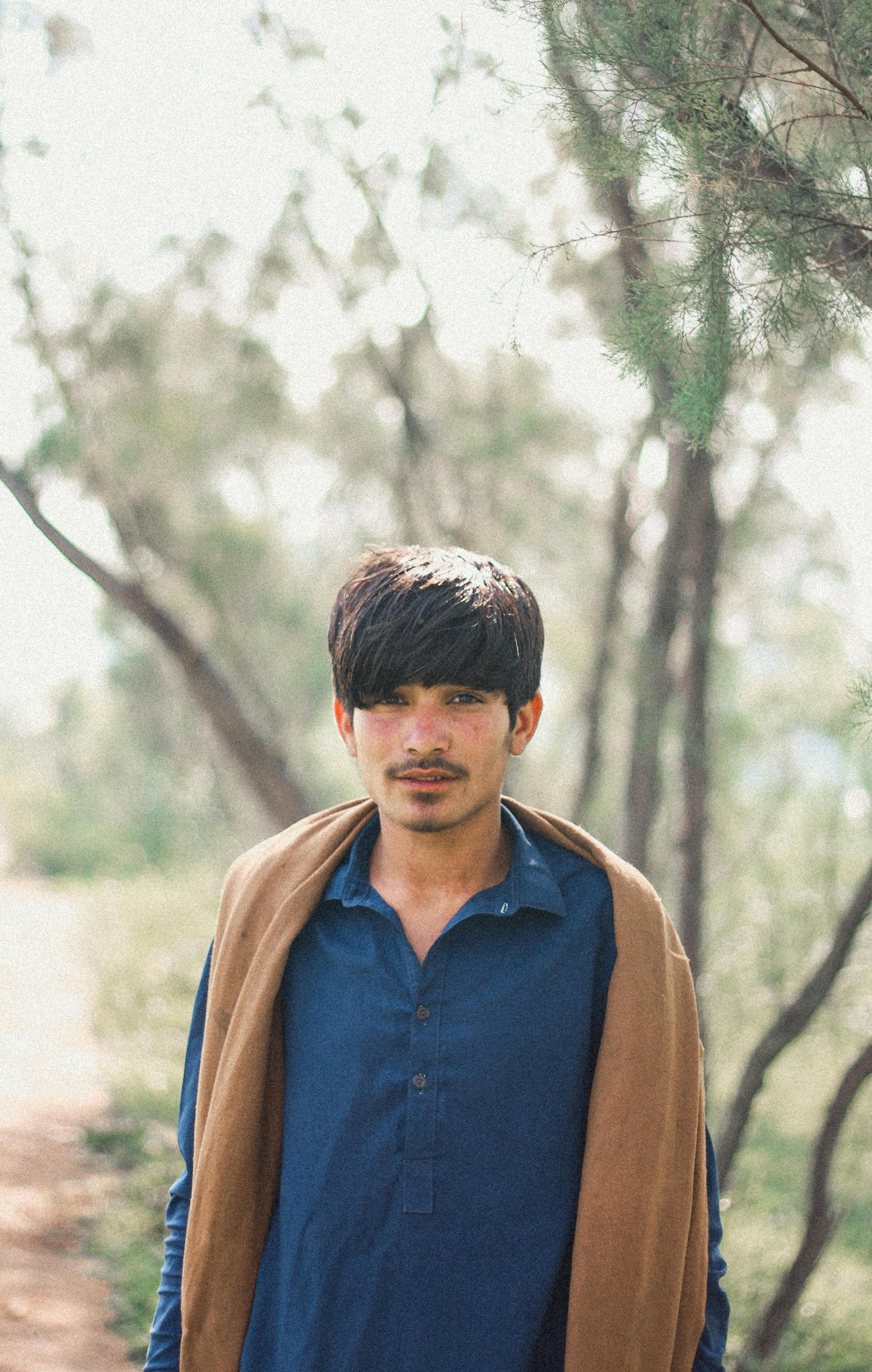 Portrait of a young man standing outdoors in Peshawar, surrounded by trees.