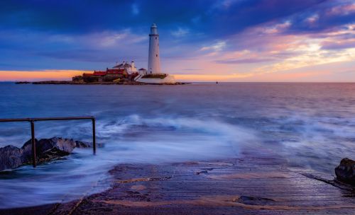 Free A scenic lighthouse view at sunset with waves crashing on the shore. Stock Photo