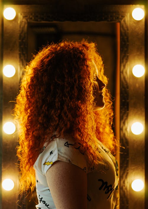 Фотография сбоку девушки, стоящей возле косметического зеркала