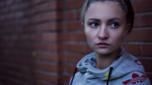 Makroaufnahme Der Frau Im Grauen Adidas Pullover über Hoodie In Der Nähe Der Backsteinmauer