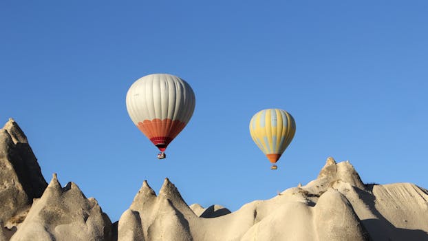 Vibrant hot air balloons soar over Cappadocia's unique rock formations under a clear blue sky.
