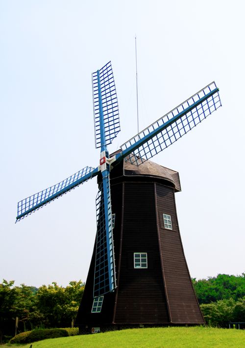 Free Charming wooden windmill against a bright sky, surrounded by lush greenery. Stock Photo