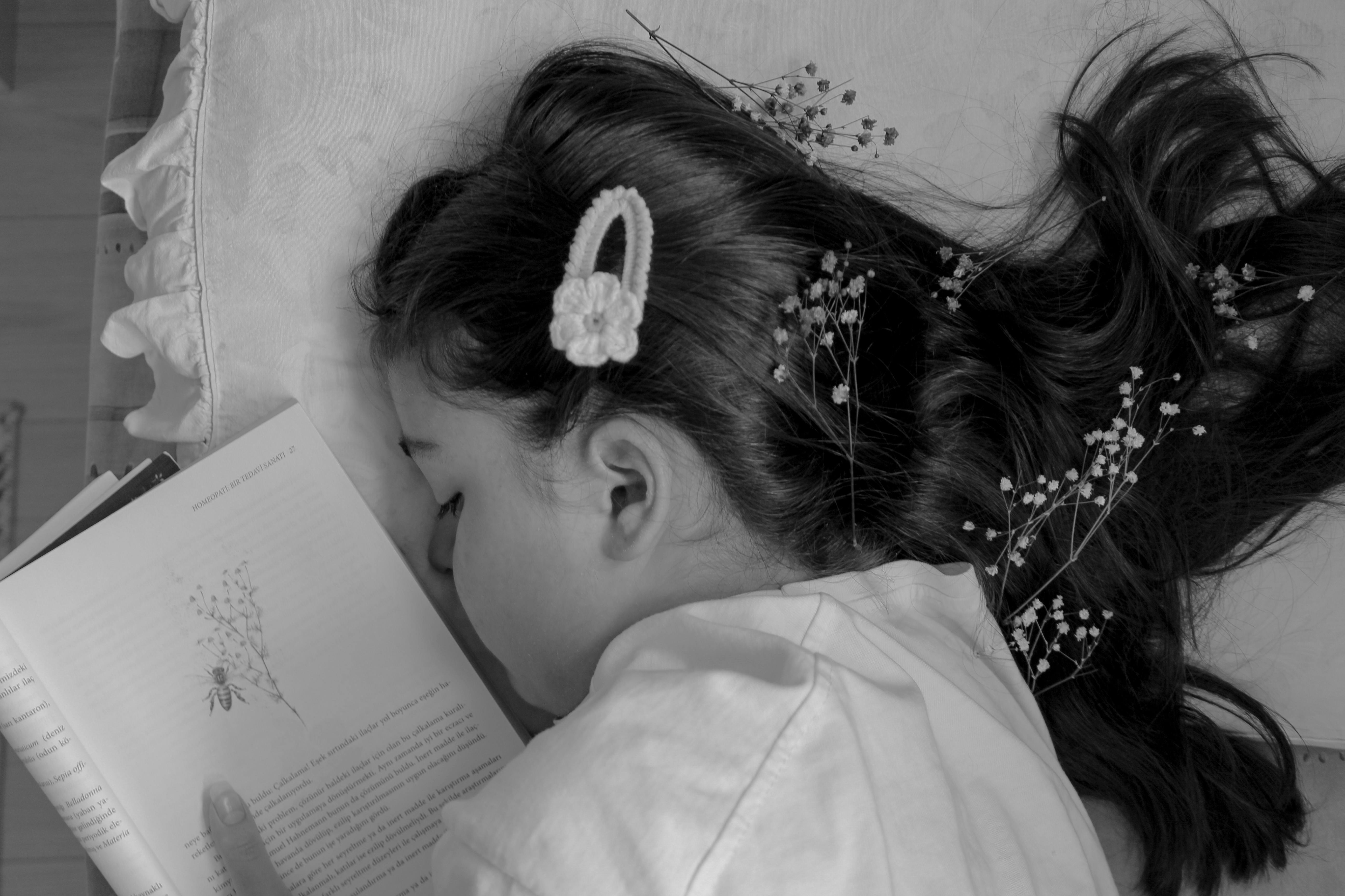 A serene black and white photo of a girl resting with a book and flowers in her hair.
