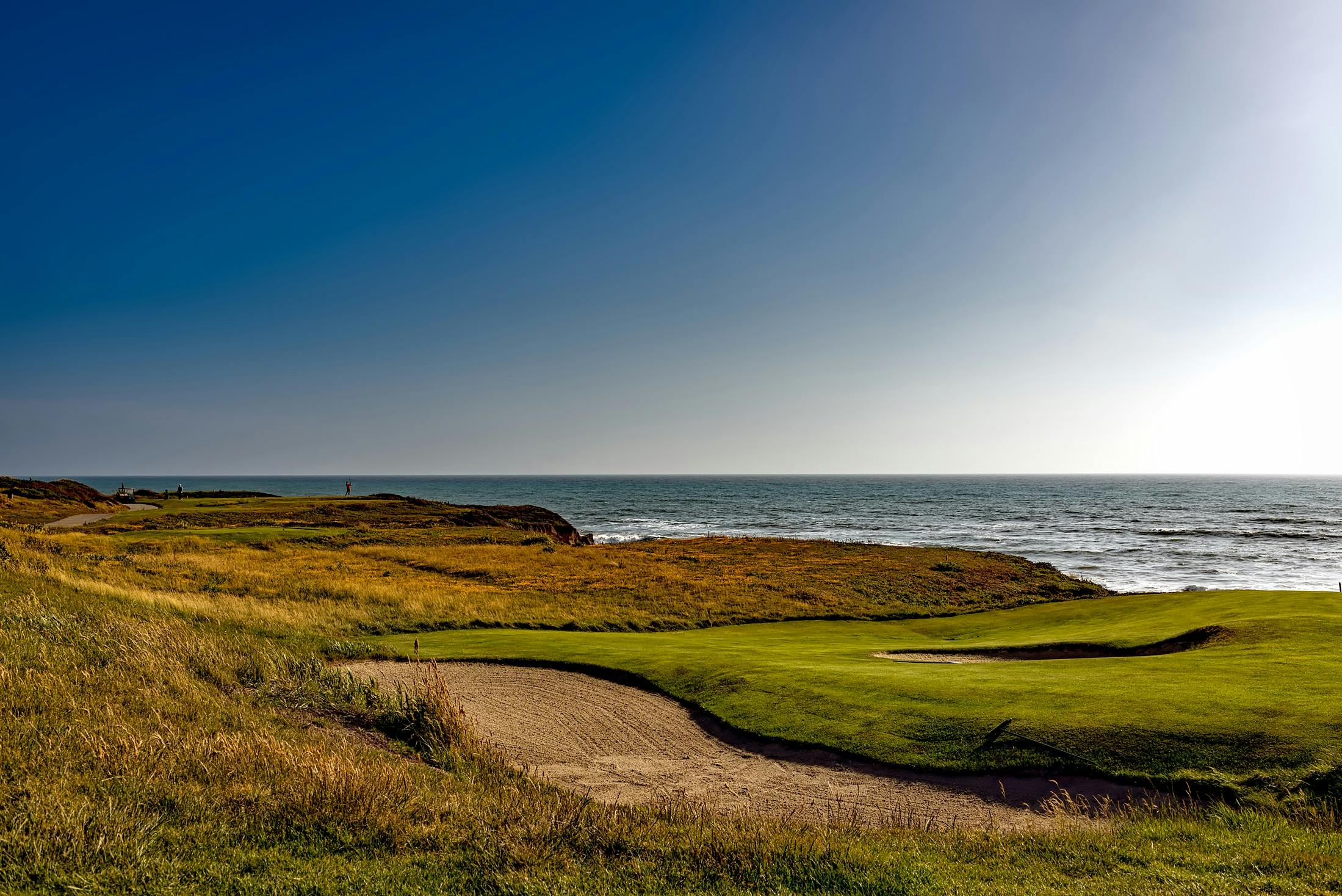 Breathtaking view of a golf course along the coastline under a clear blue sky.