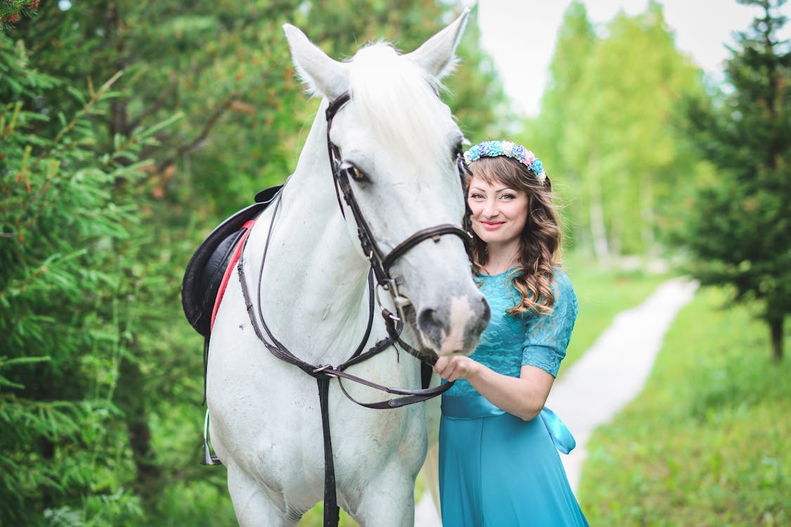 免費 站立在白馬旁邊的藍色禮服的微笑的婦女 圖庫相片