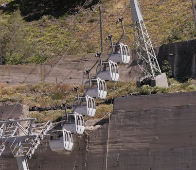 Mountain cable cars ascending a steep incline in a scenic rural landscape, surrounded by greenery