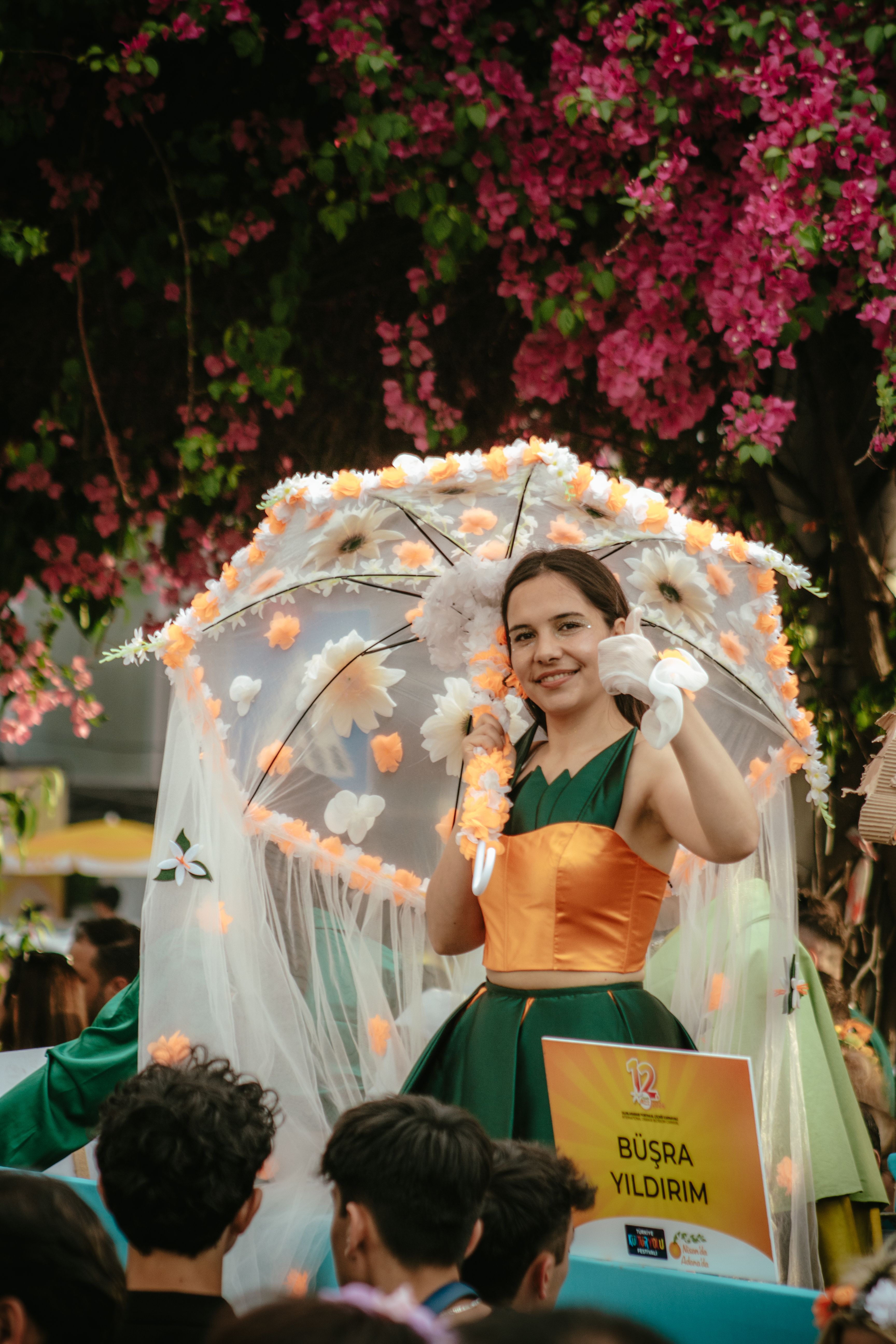 A vibrant parade scene in Adana with a woman in costume holding an umbrella.