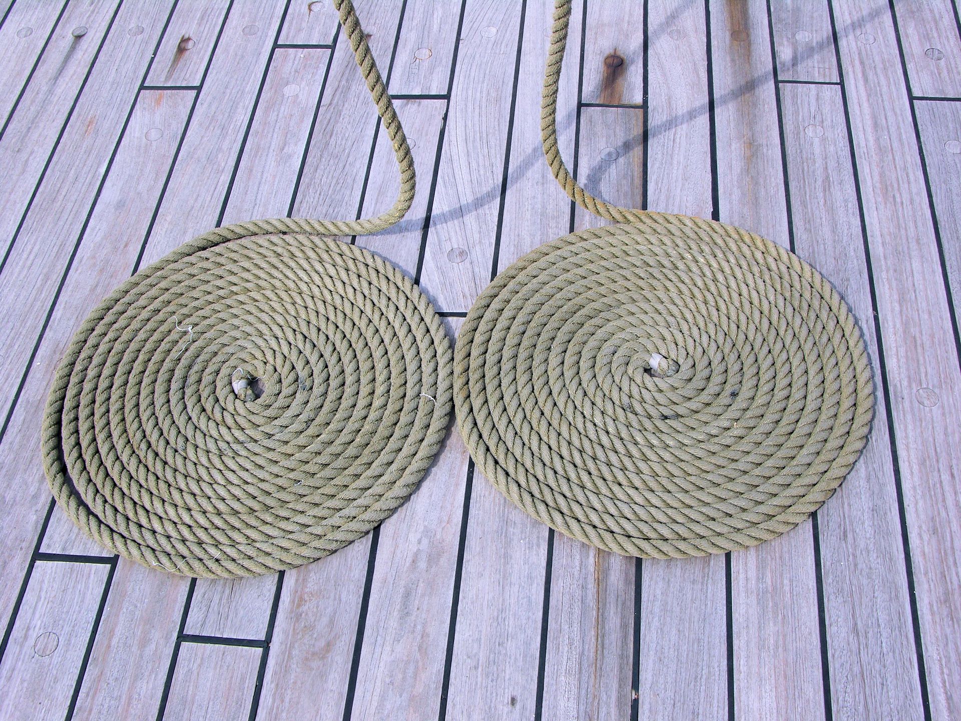 Two neatly coiled ropes on a wooden deck create a rustic nautical pattern.
